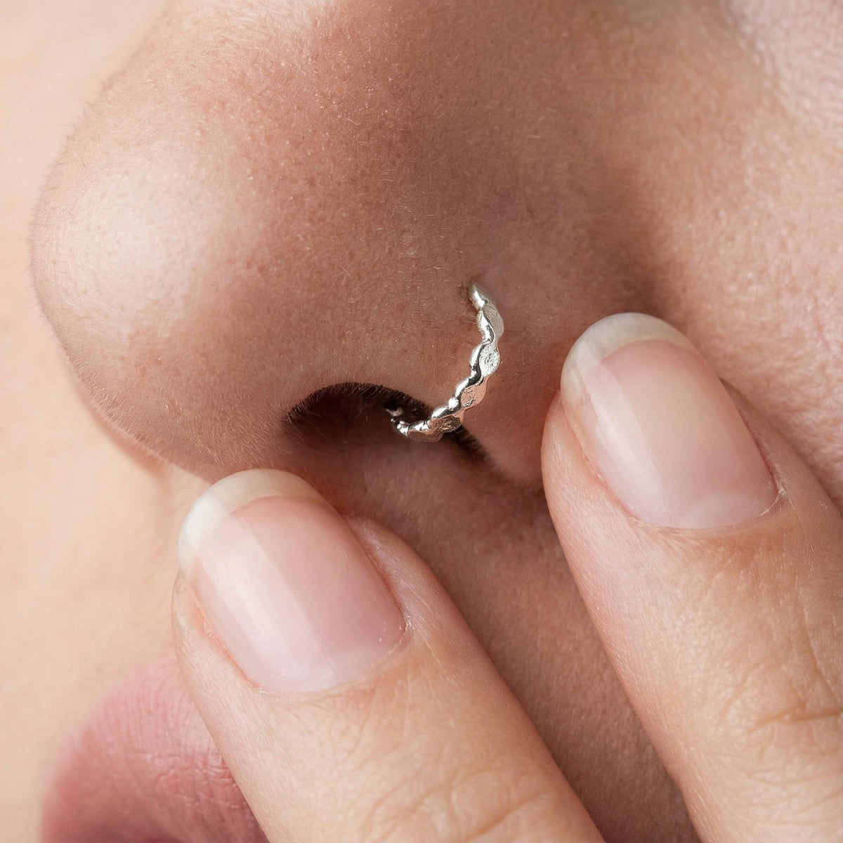 A close-up of a person's nose with a silver nose ring, and the person's fingers are visible.