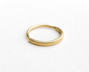 A gold ring with a thin, textured band is shown against a plain white background.