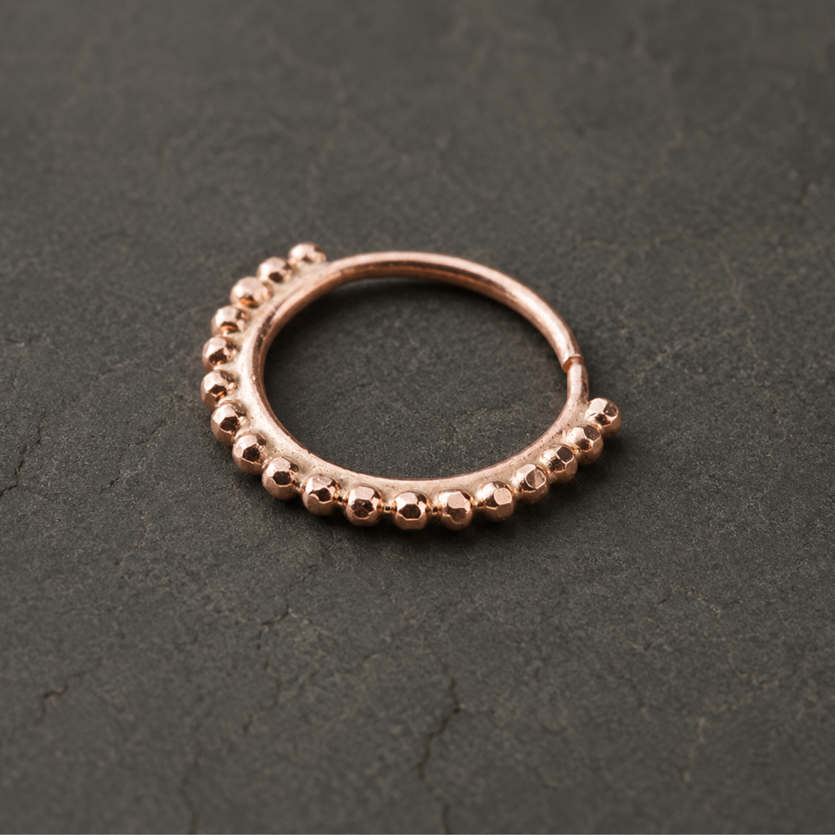 A copper-colored metal ring with a row of small, round beads or stones along the edge, resting on a dark surface.