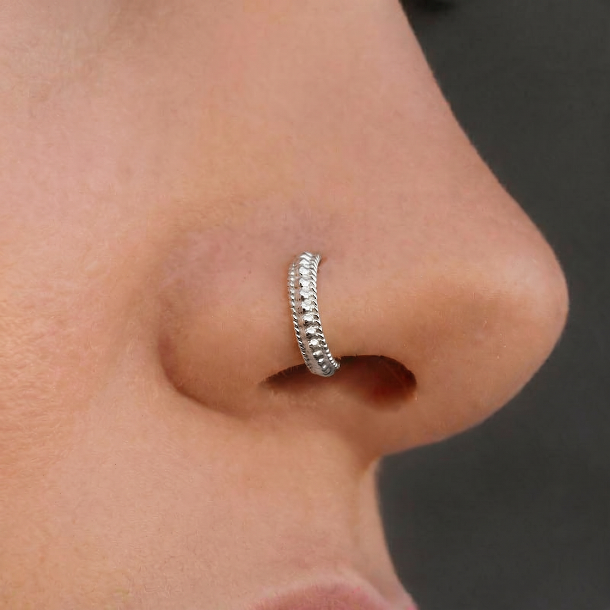 A close-up of a person's nose with a decorative metal ring on it.
