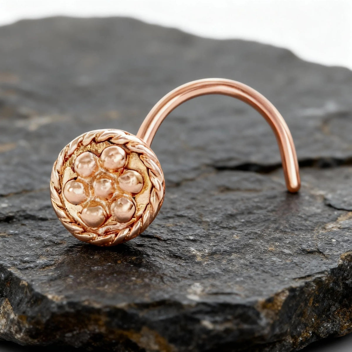 A copper-colored nose ring with a circular design sits on a dark gray rock.