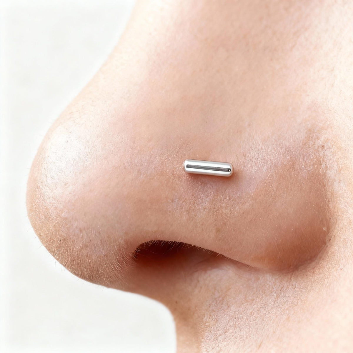 A close-up of a person's nose with a small silver metal object, possibly a piercing, inserted into it.
