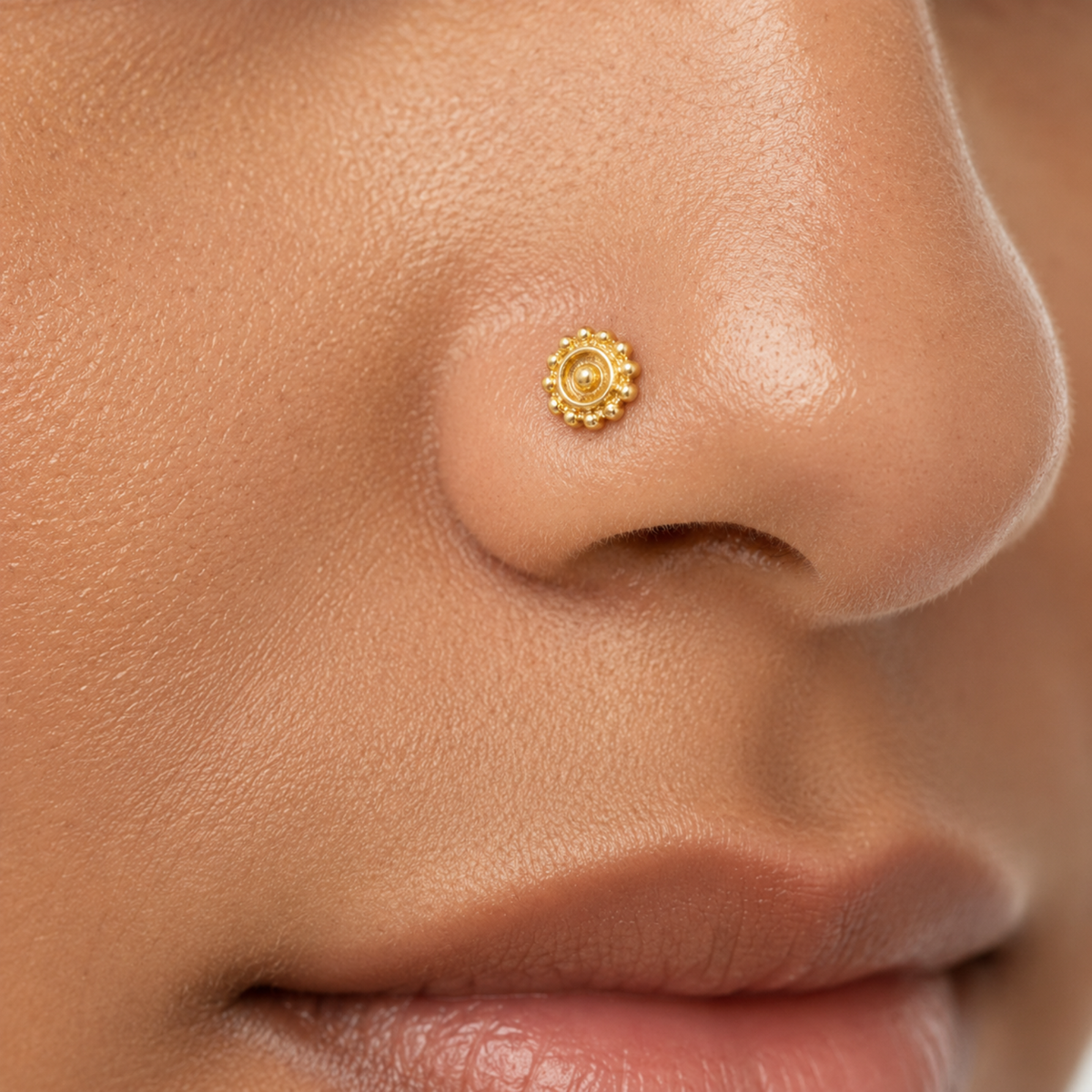 A close-up of a person's nose with a small, ornate gold nose ring.