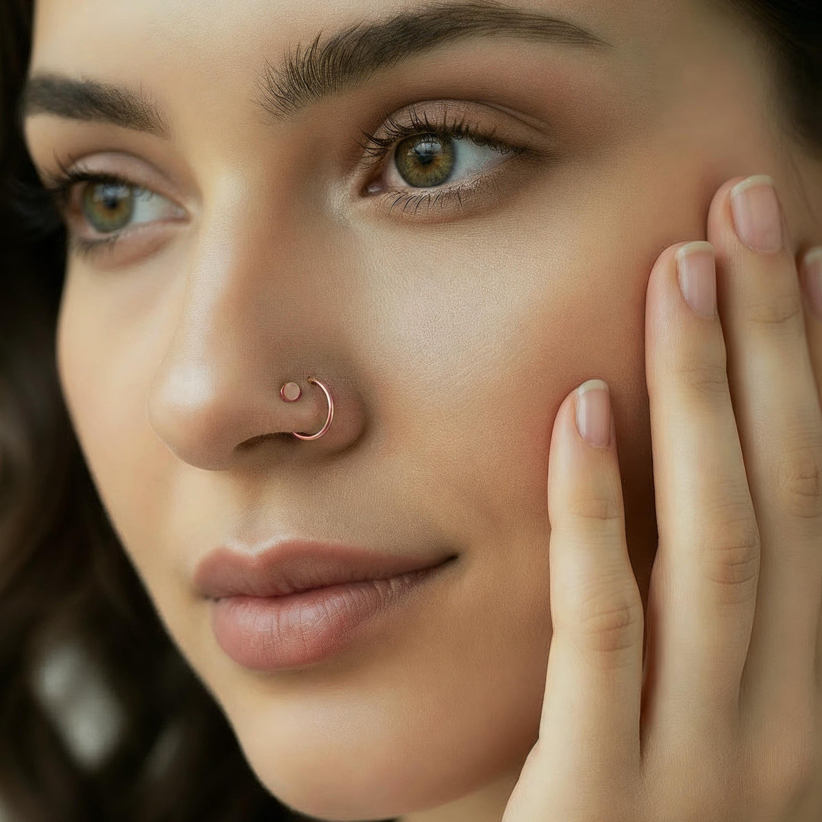 A close-up portrait of a woman with a nose ring, her hand gently resting on her face.