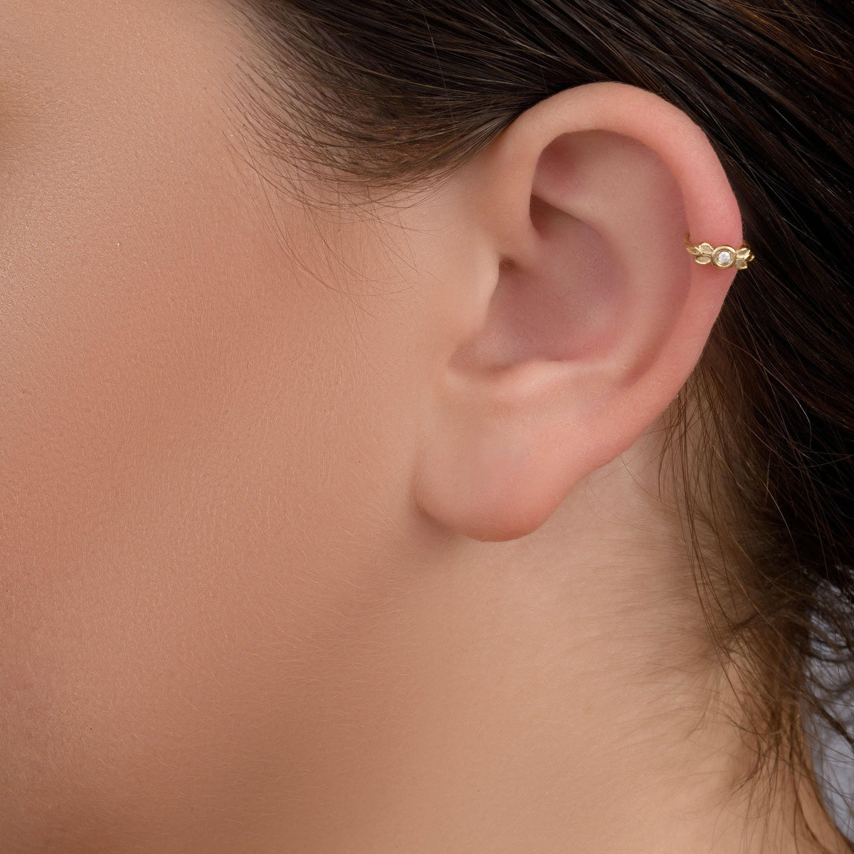 A close-up of a person's ear with a gold earring featuring a small gemstone.