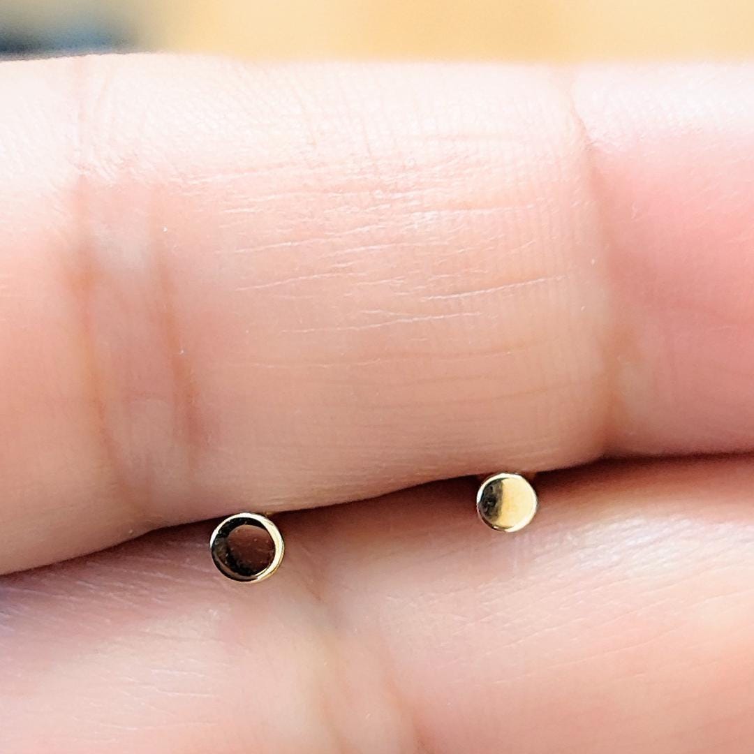 A close-up image of a person's fingers holding two small gold-colored earrings.