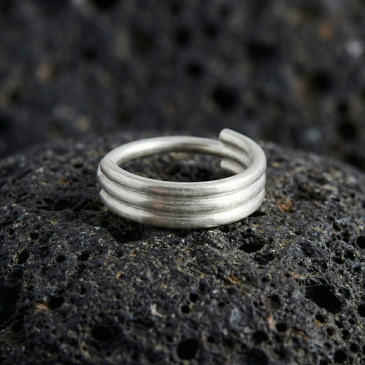 A silver ring with three concentric rings is resting on a dark, rocky surface.