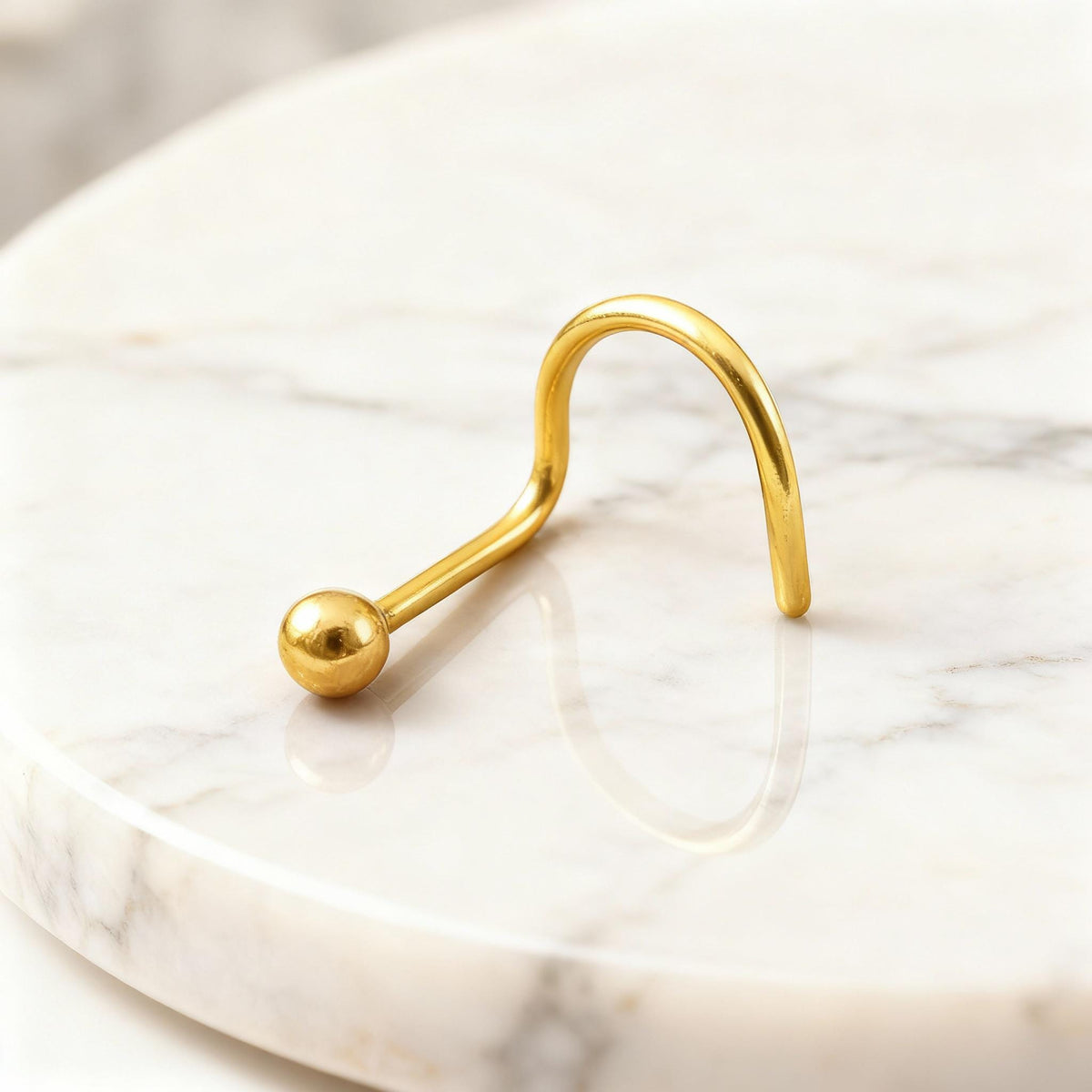A gold-colored metal nose ring is resting on a white marble surface.
