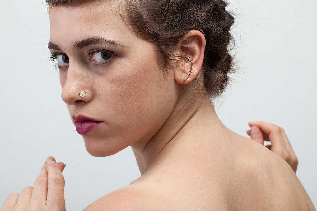 A woman with a nose ring and a serious expression on her face, with her hands behind her back.
