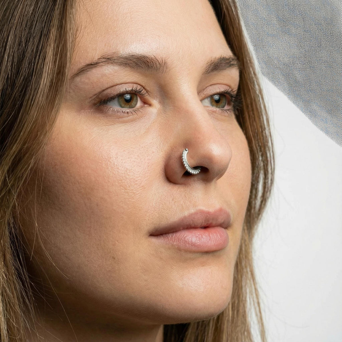 A close-up portrait of a woman with a nose ring, looking pensively to the side.