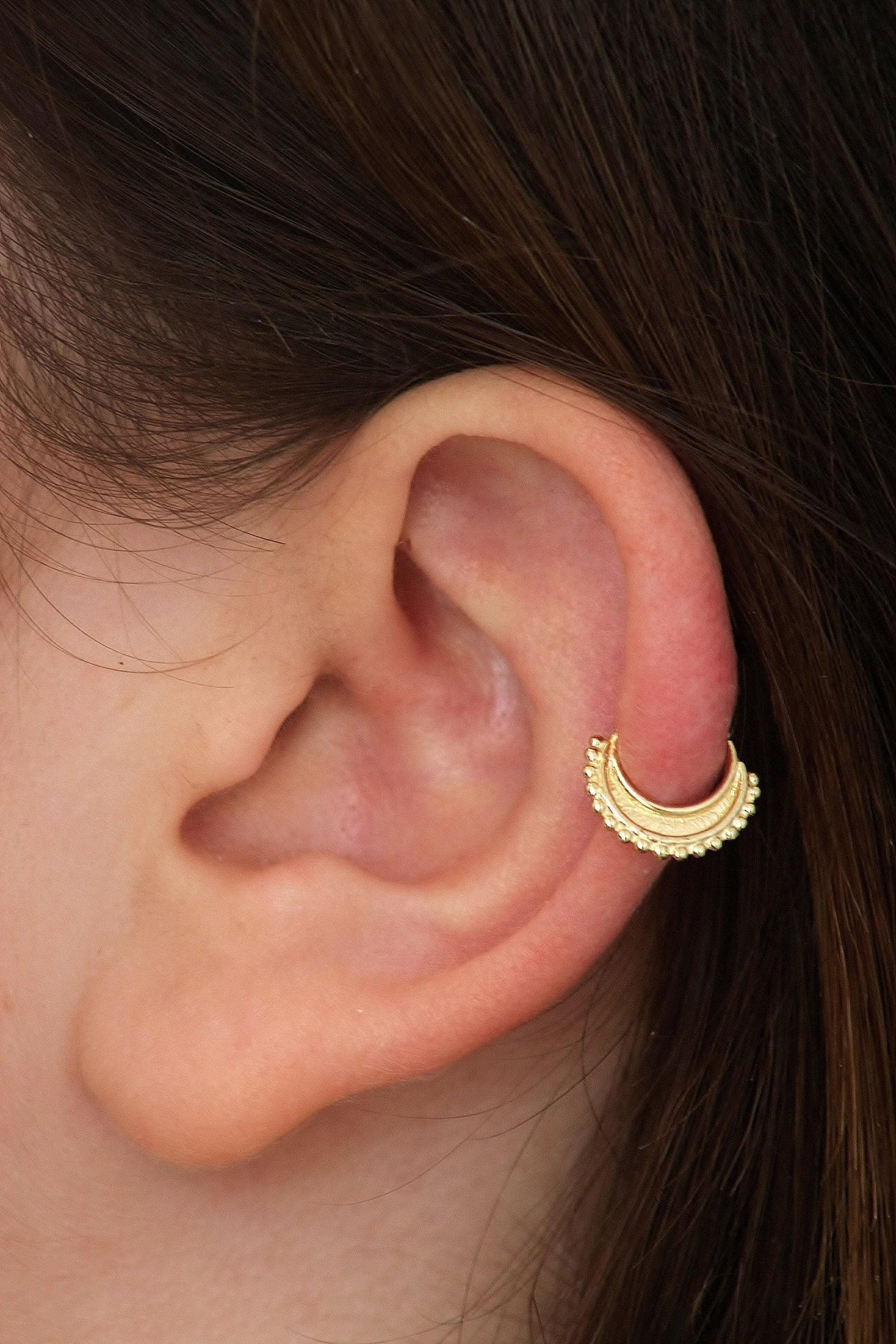A close-up of a person's ear with a gold earring in the earlobe.