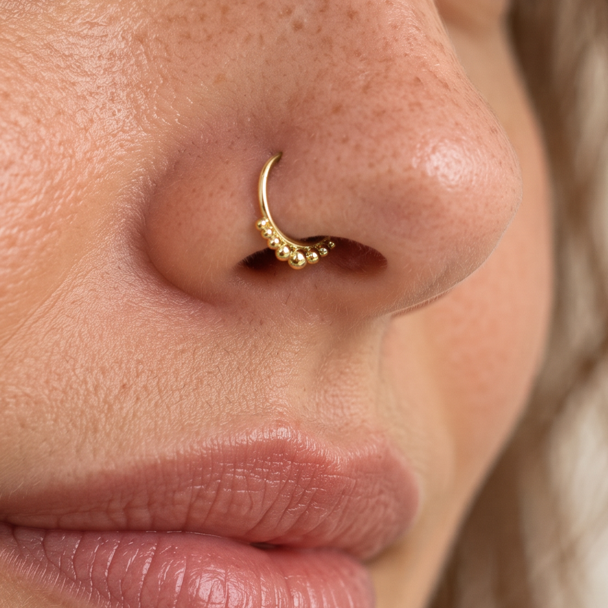 A close-up of a person's nose with a gold nose ring featuring a decorative element.