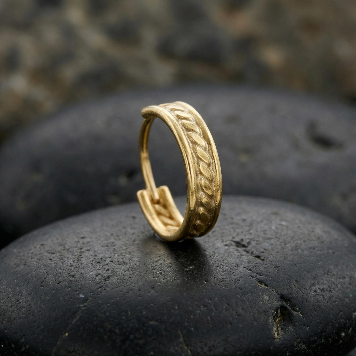 A gold earring with a twisted design sits on a black rock.