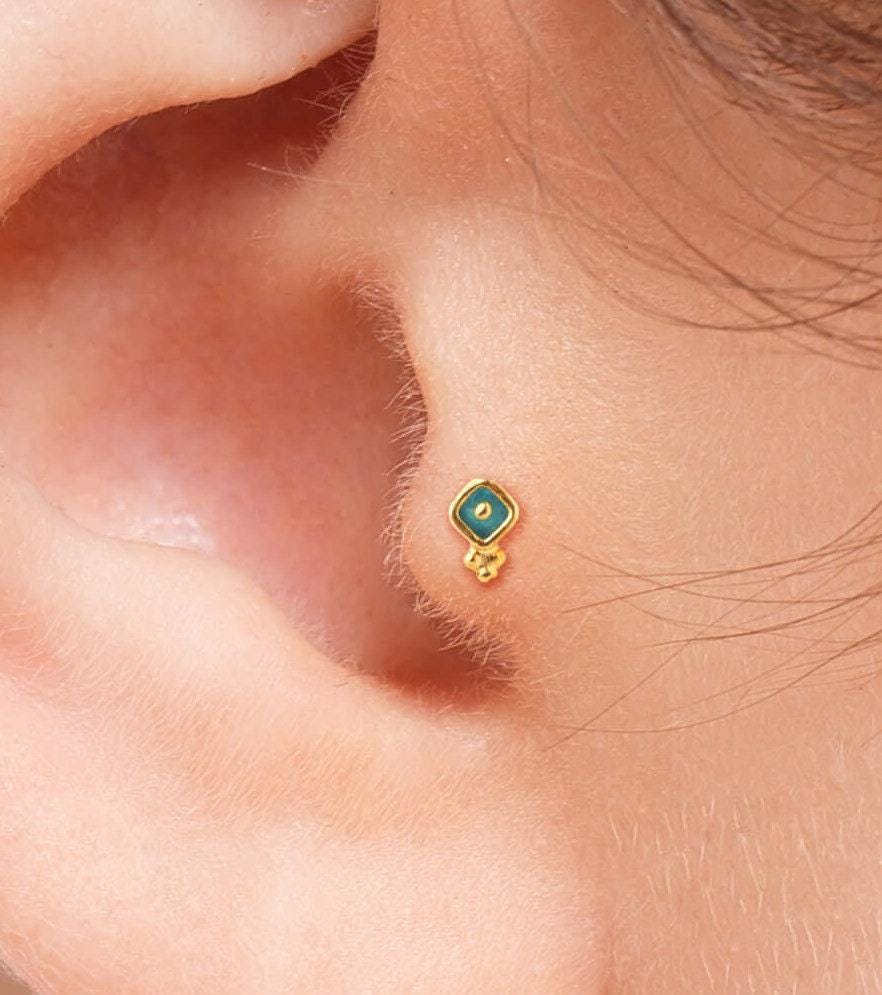 Tragus Piercing Earring: A close-up view of a person's ear, showing a small gold earring with a green gemstone in the earlobe.