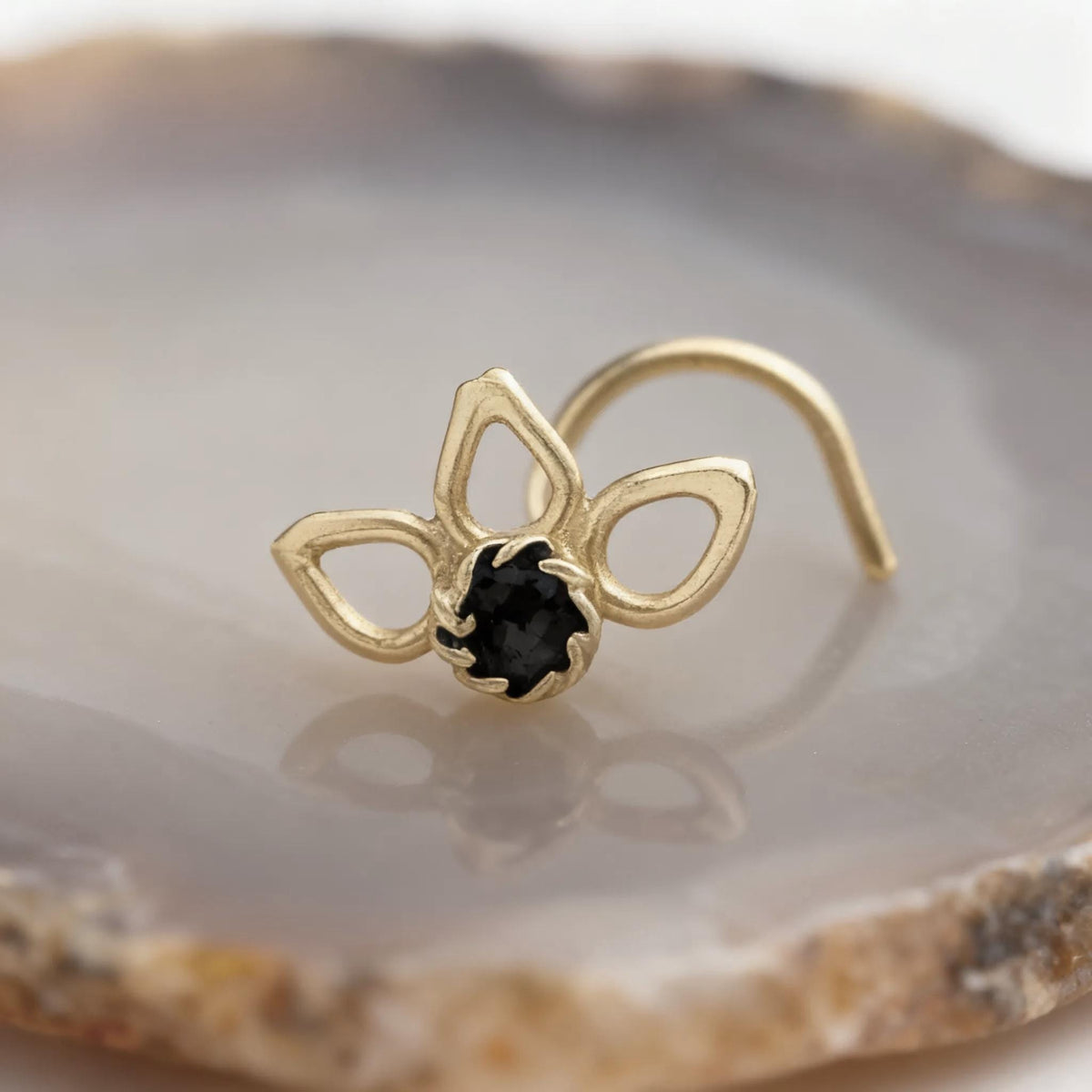 A gold-colored nose ring with a black gemstone is displayed on a stone or rock surface.