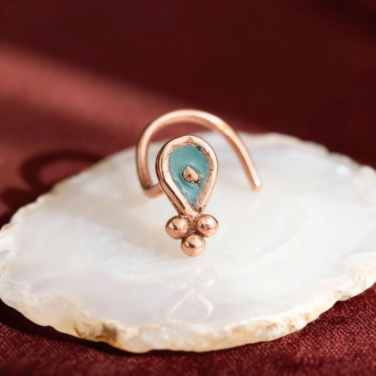 A copper-colored nose ring with a turquoise stone is displayed on a white stone or rock.