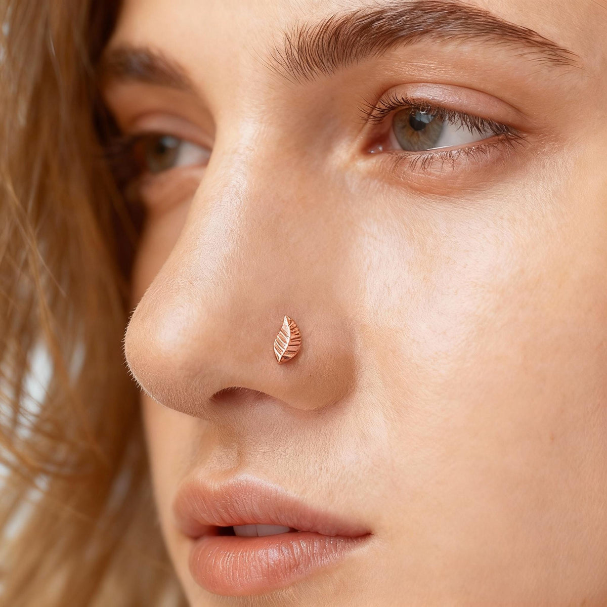 A close-up of a woman's face, focusing on her nose and the small leaf-shaped nose ring.