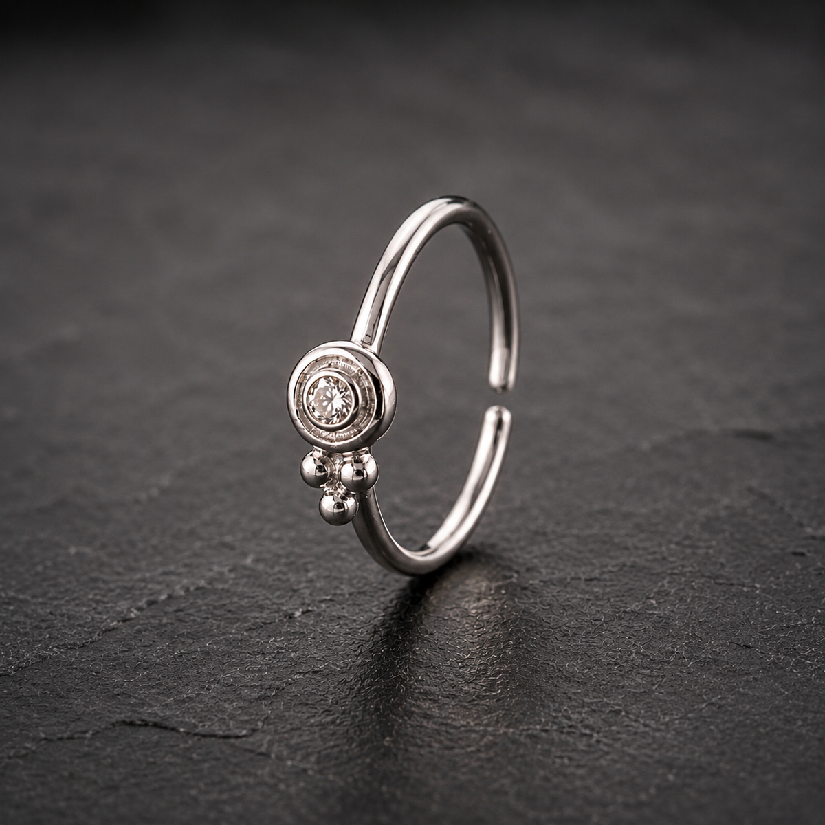 A silver ring with a small diamond in the center is displayed against a dark background.