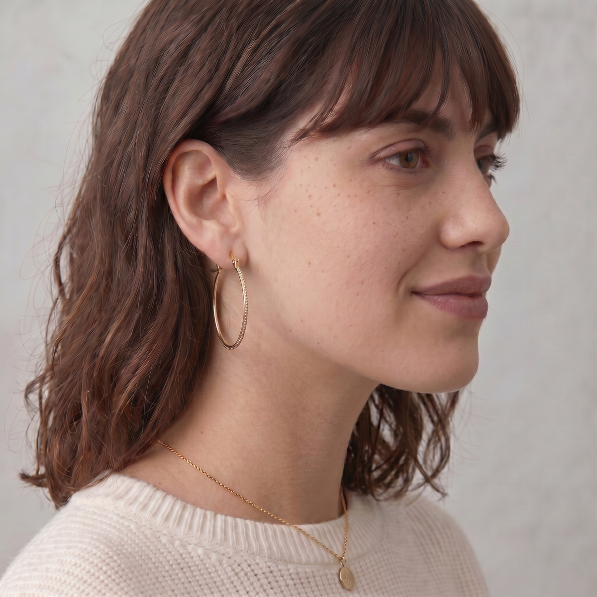 A woman with long brown hair wearing a white sweater and gold hoop earrings, smiling at the camera.