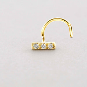 Minimal Diamond Bar Nose Stud: A gold-colored nose ring with three small diamonds set in the center.