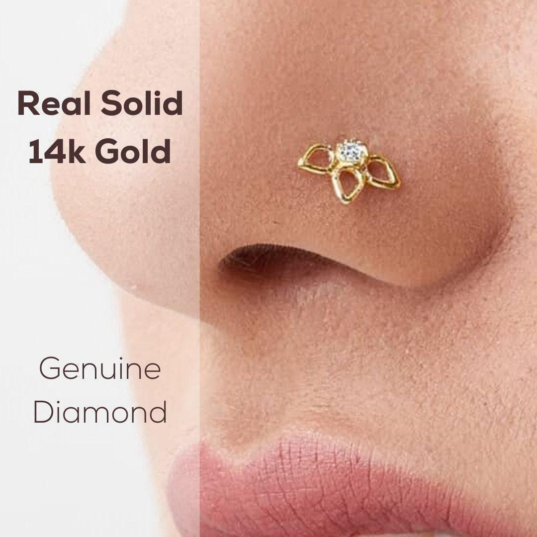 a close-up of a person's nose with a 14k gold nose ring featuring a diamond-like gemstone.