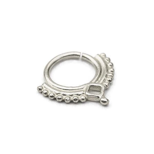 A silver-colored metal ring with a decorative design, featuring a central square-shaped element surrounded by a row of small, round beads or stones.