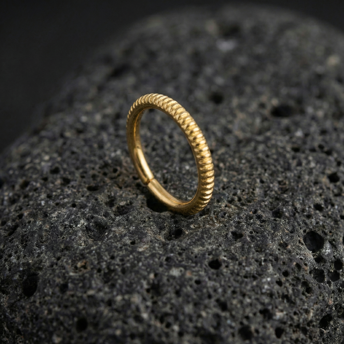 A gold ring with a twisted design sits on a dark, textured surface.