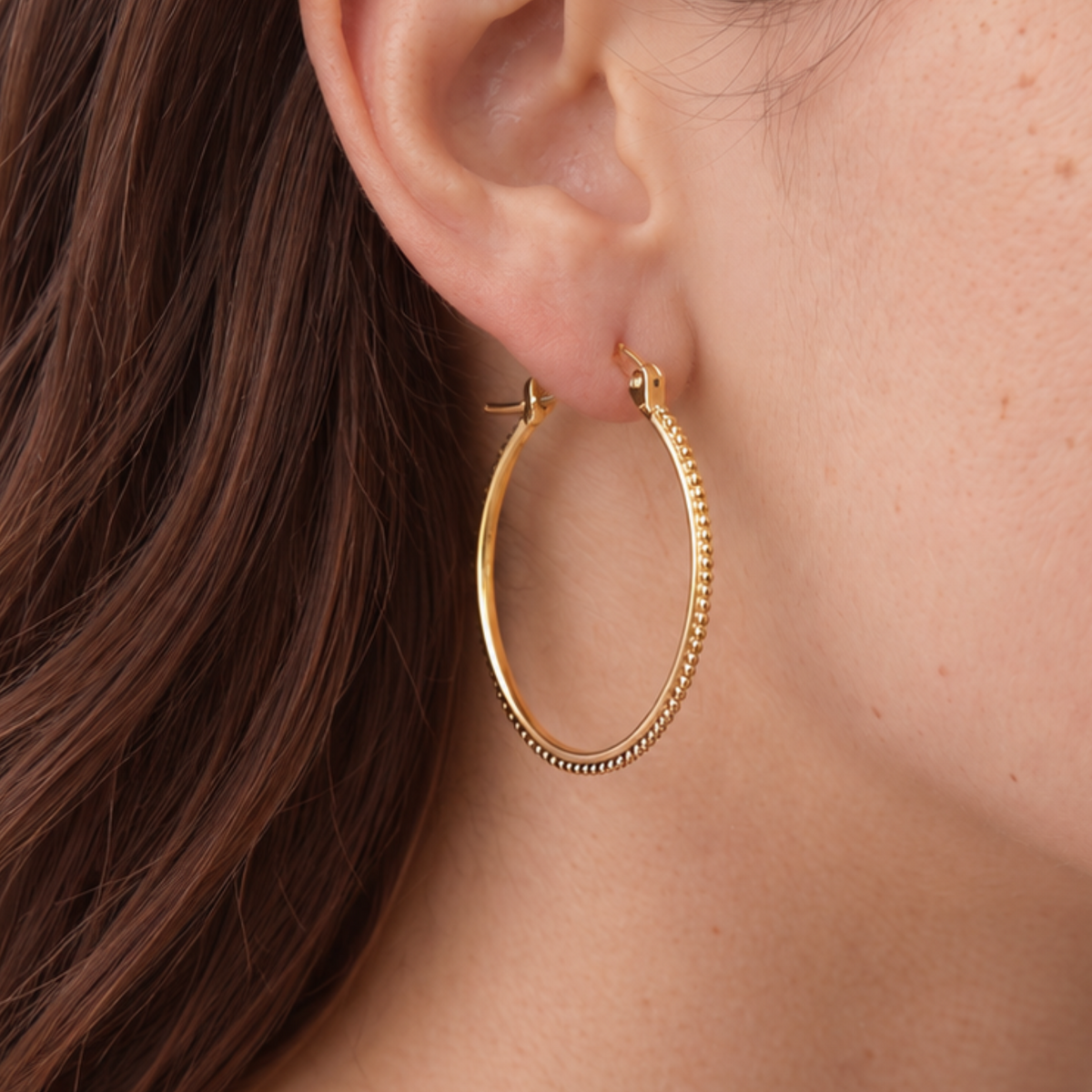 A close-up view of a person's ear wearing a gold hoop earring.