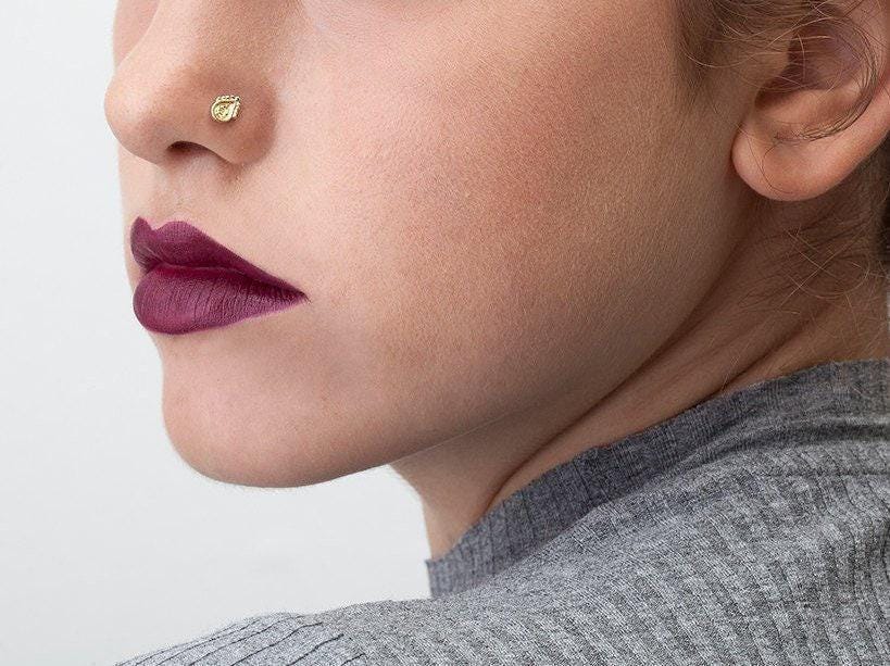 A close-up of a person's face, focusing on their nose and lips, with a gold nose stud visible.