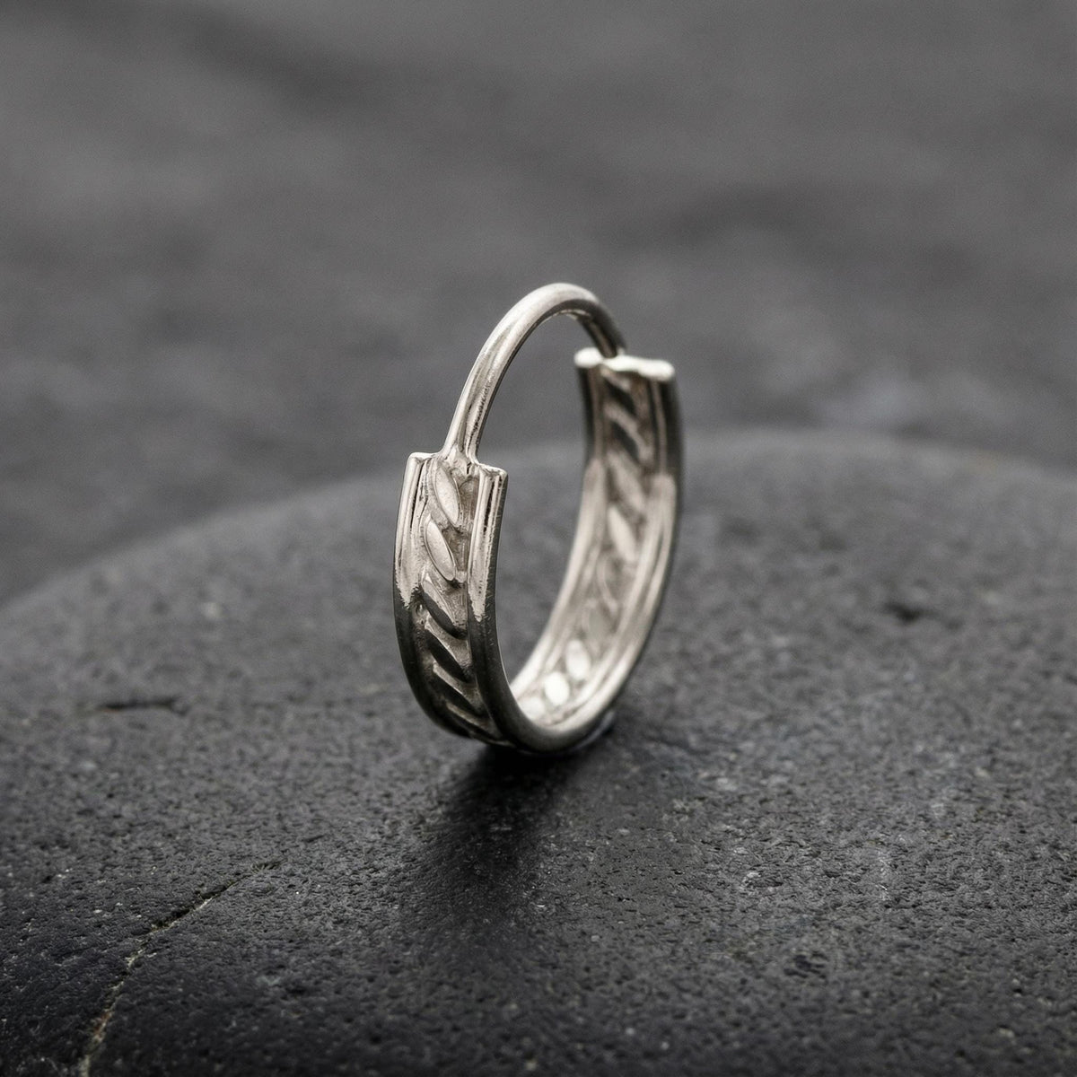 A silver hoop earring with a decorative design rests on a dark surface.