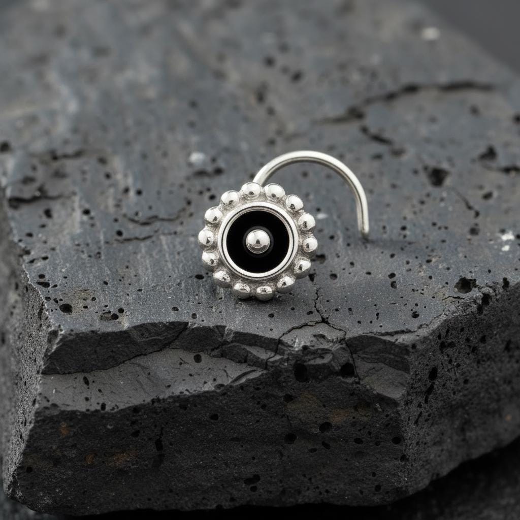 A silver nose ring with a black center is resting on a dark, rocky surface.