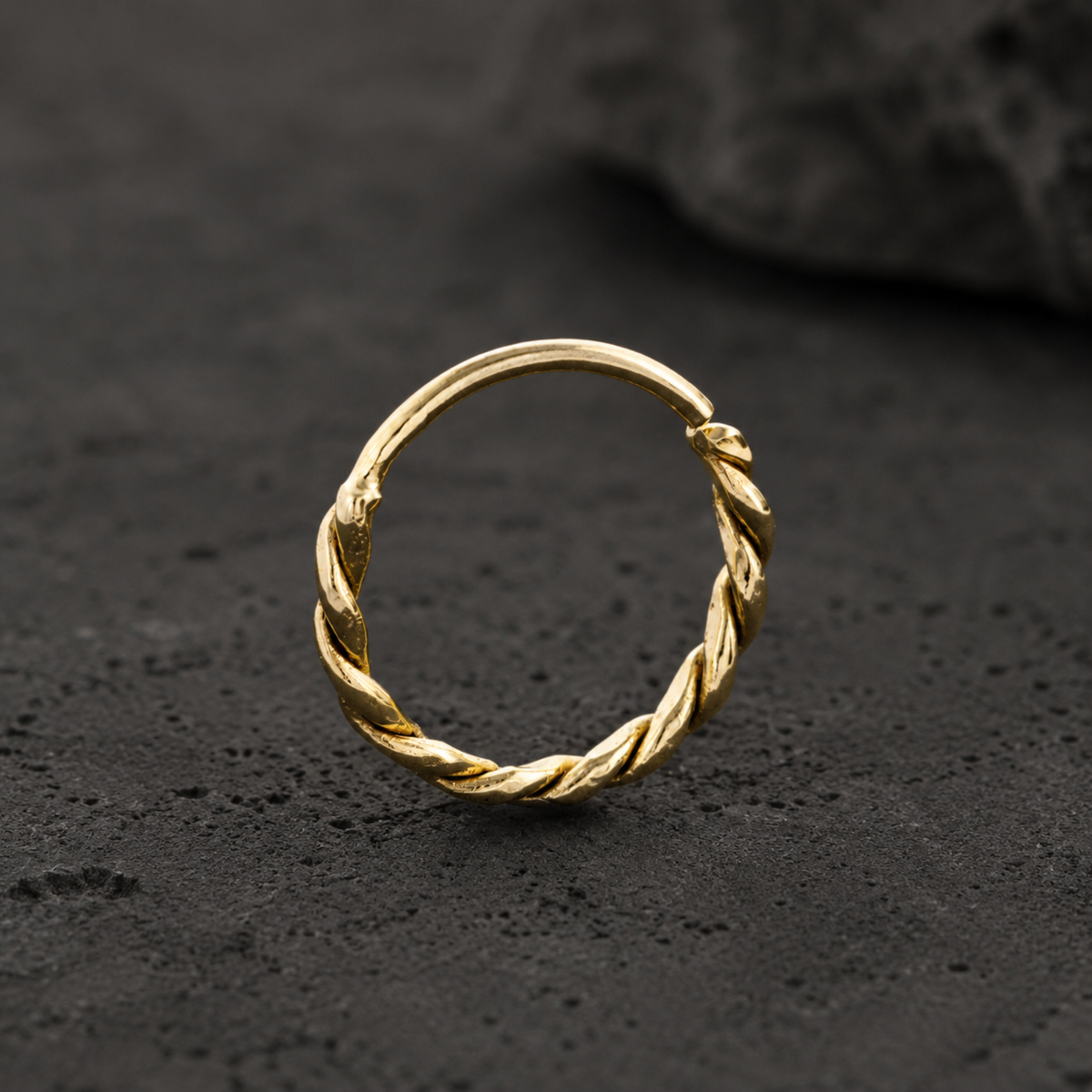 A gold-colored ring with a twisted design sits on a dark surface.