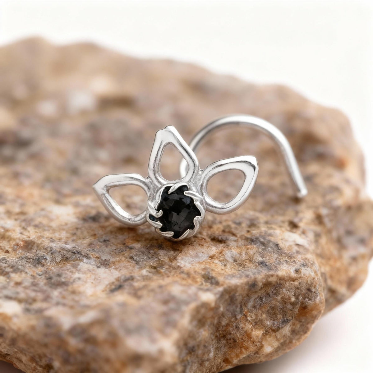 A silver nose ring with a black gemstone is placed on a rock.