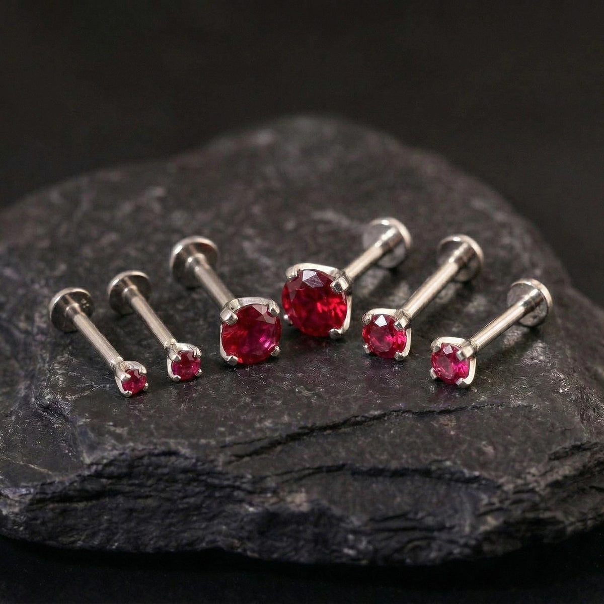 A collection of red gemstone earrings is displayed on a dark surface, with the earrings varying in size and shape.
