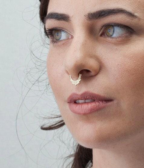 A close-up of a woman's face, focusing on her nose and lips, with a gold nose ring visible.