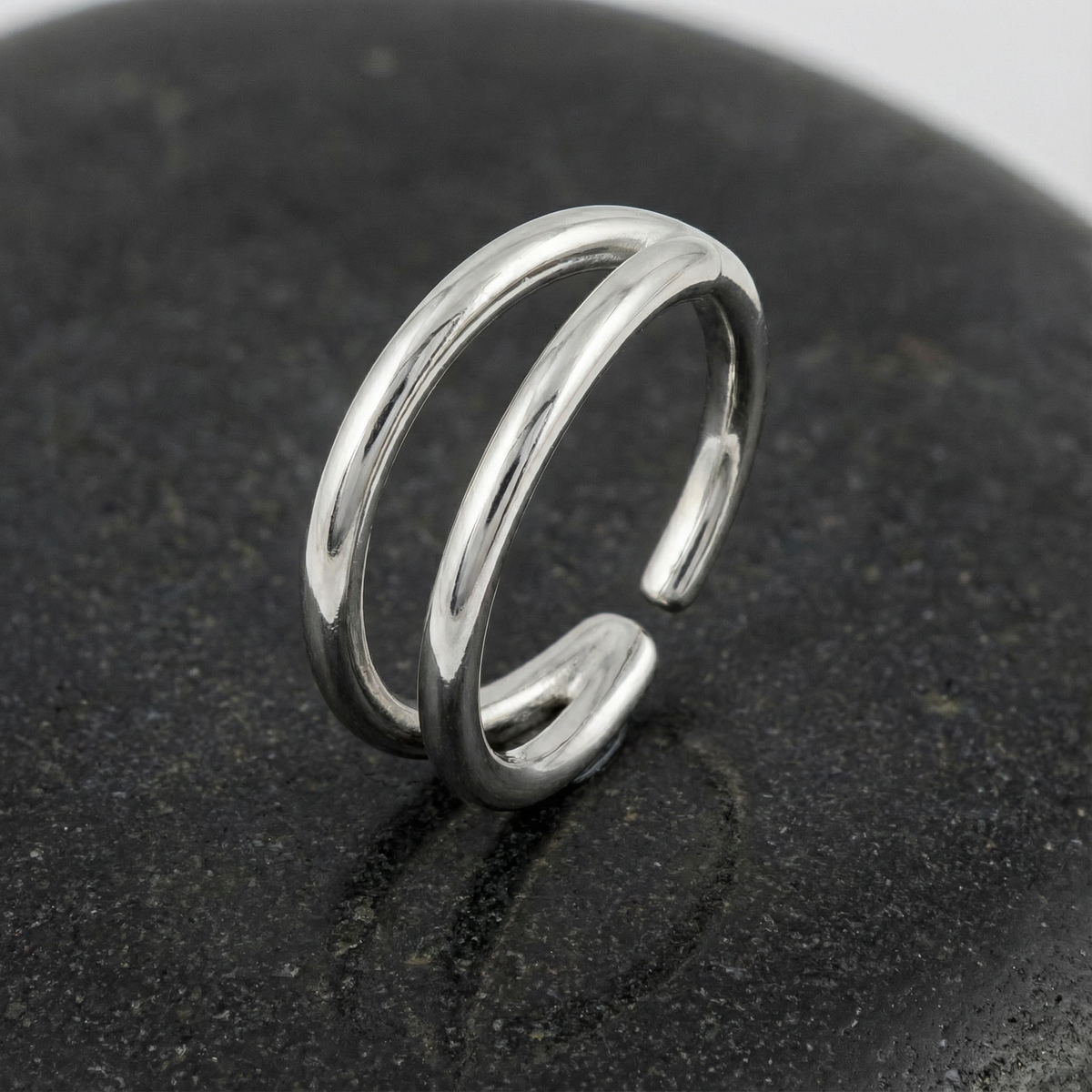 A silver ring with a unique, double-ended design is resting on a black surface.