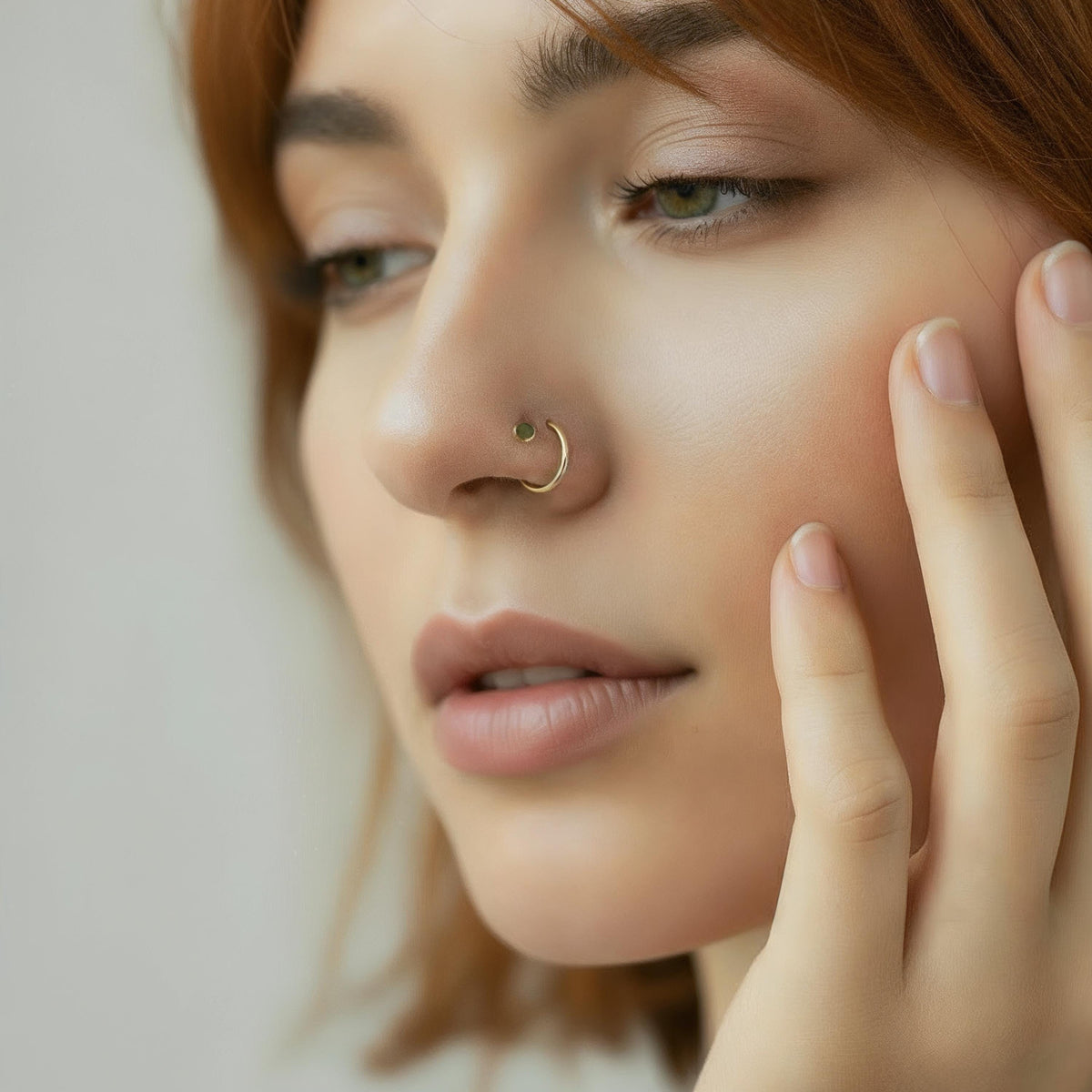A close-up portrait of a woman with a nose ring, her hand gently resting on her face.