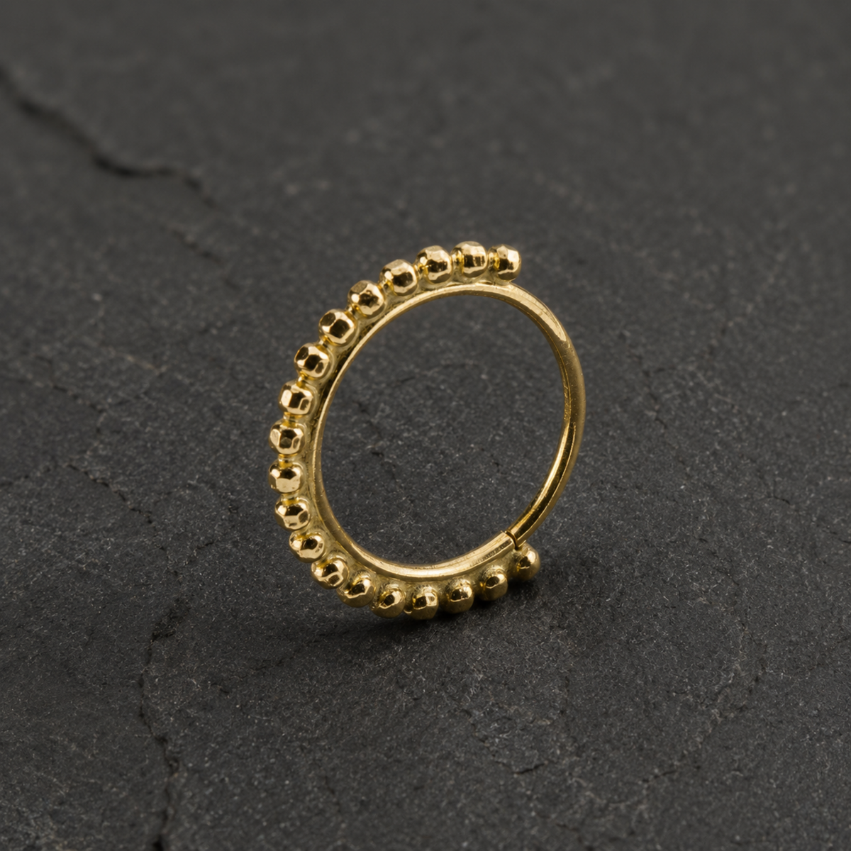 A gold-colored ring with a row of small, round beads or stones along the outer edge, resting on a dark surface.