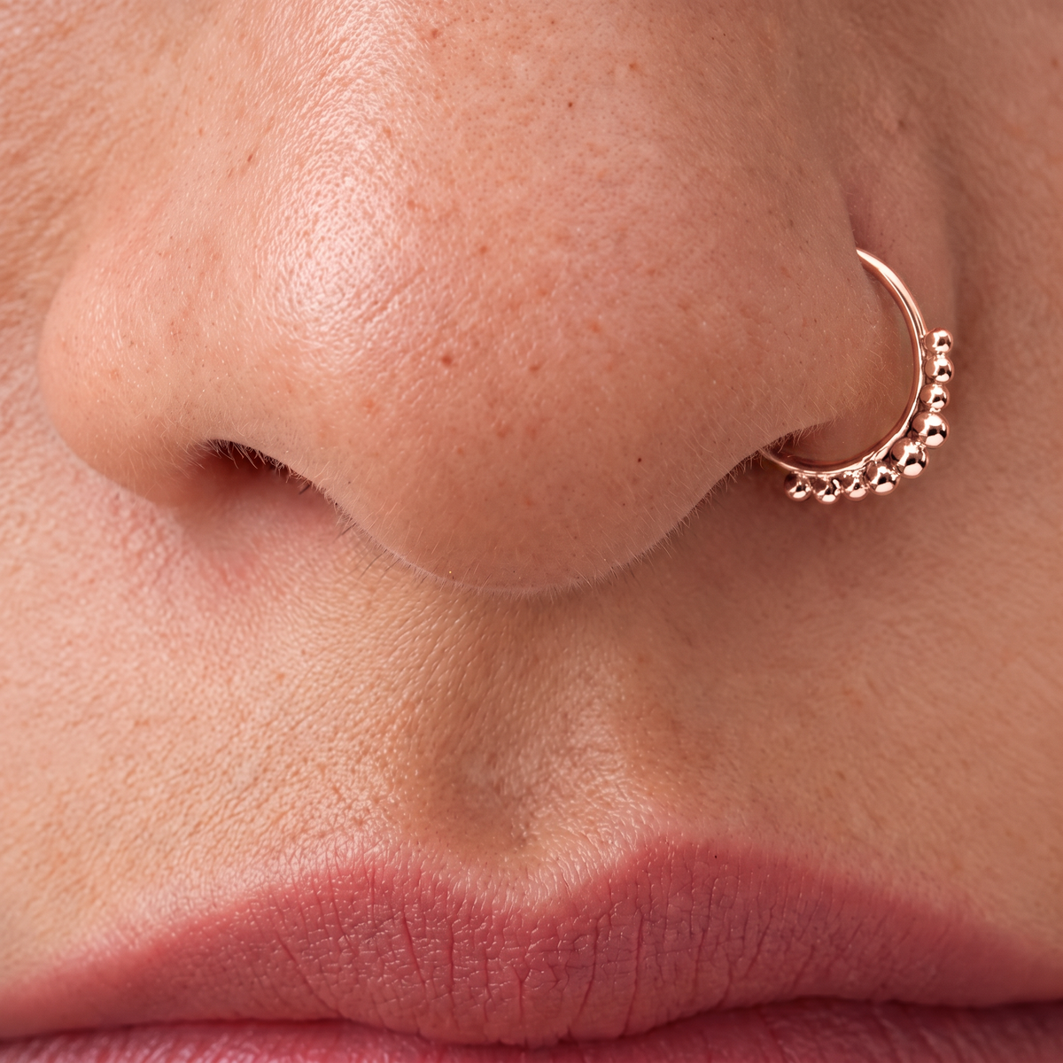A close-up of a person's nose and lips, with a gold-colored nose ring featuring small beads around the rim.