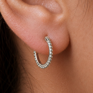A close-up view of a person's ear with a silver hoop earring featuring a row of small, round beads.