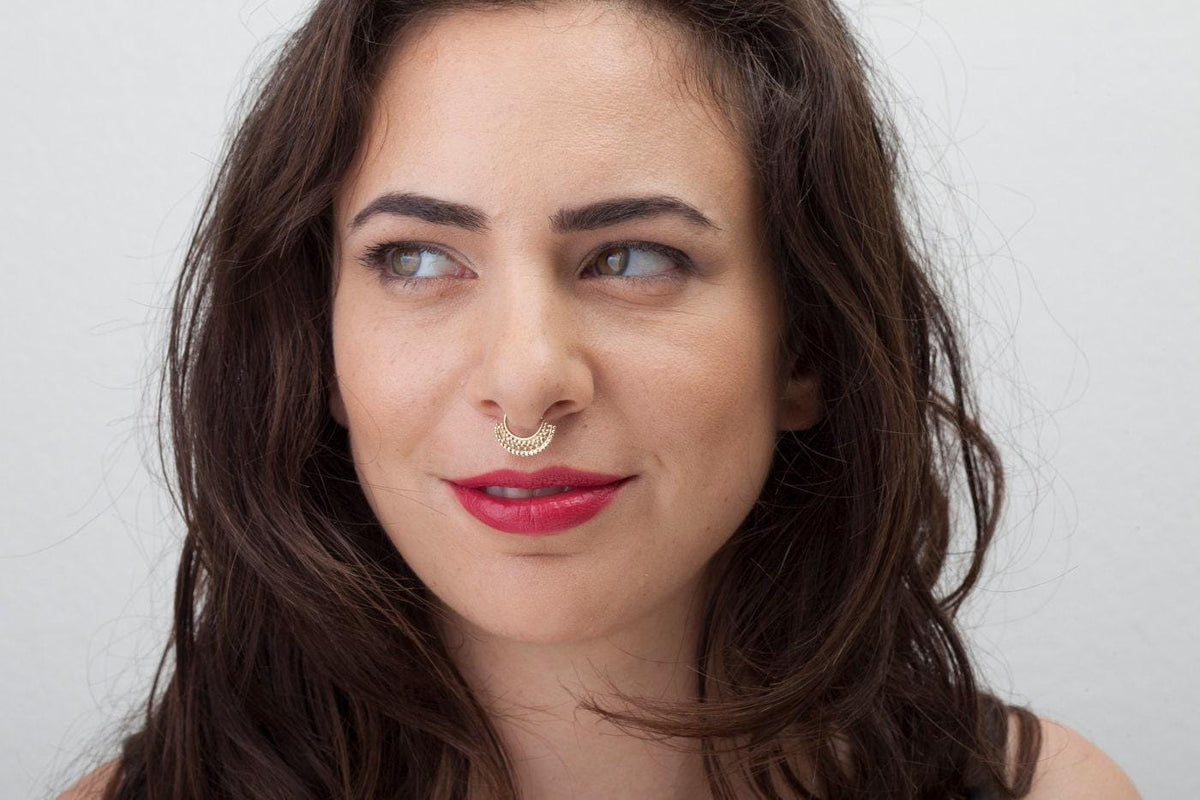 A woman with long brown hair and a nose piercing is smiling at the camera.