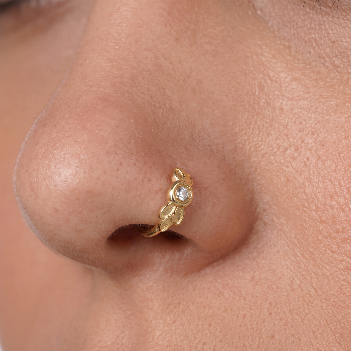 A close-up of a person's nose with a gold leaf-shaped nose ring featuring a small diamond.
