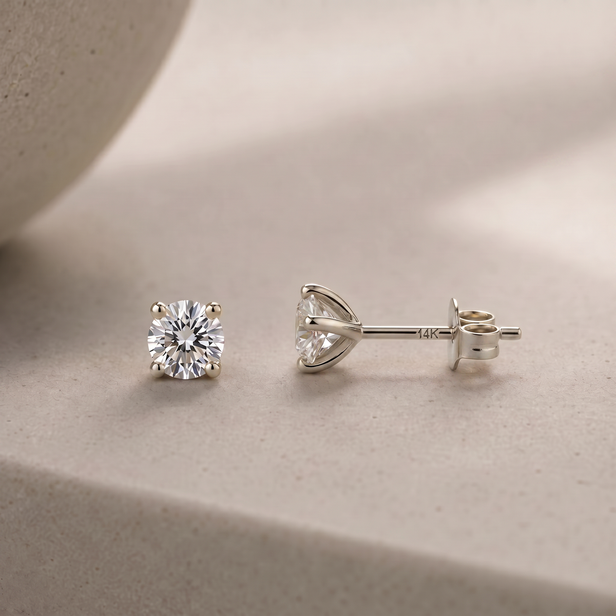 A pair of elegant diamond earrings with a large central diamond and smaller diamonds on either side rests on a light-colored surface.