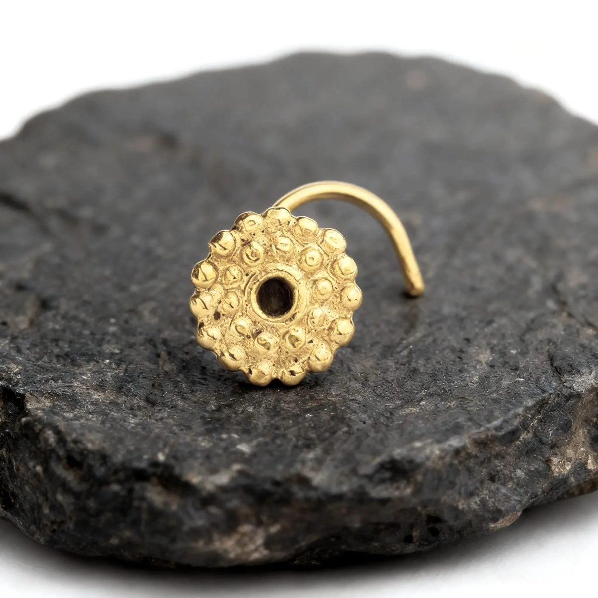 A gold-colored nose ring with a round center is resting on a dark gray rock.