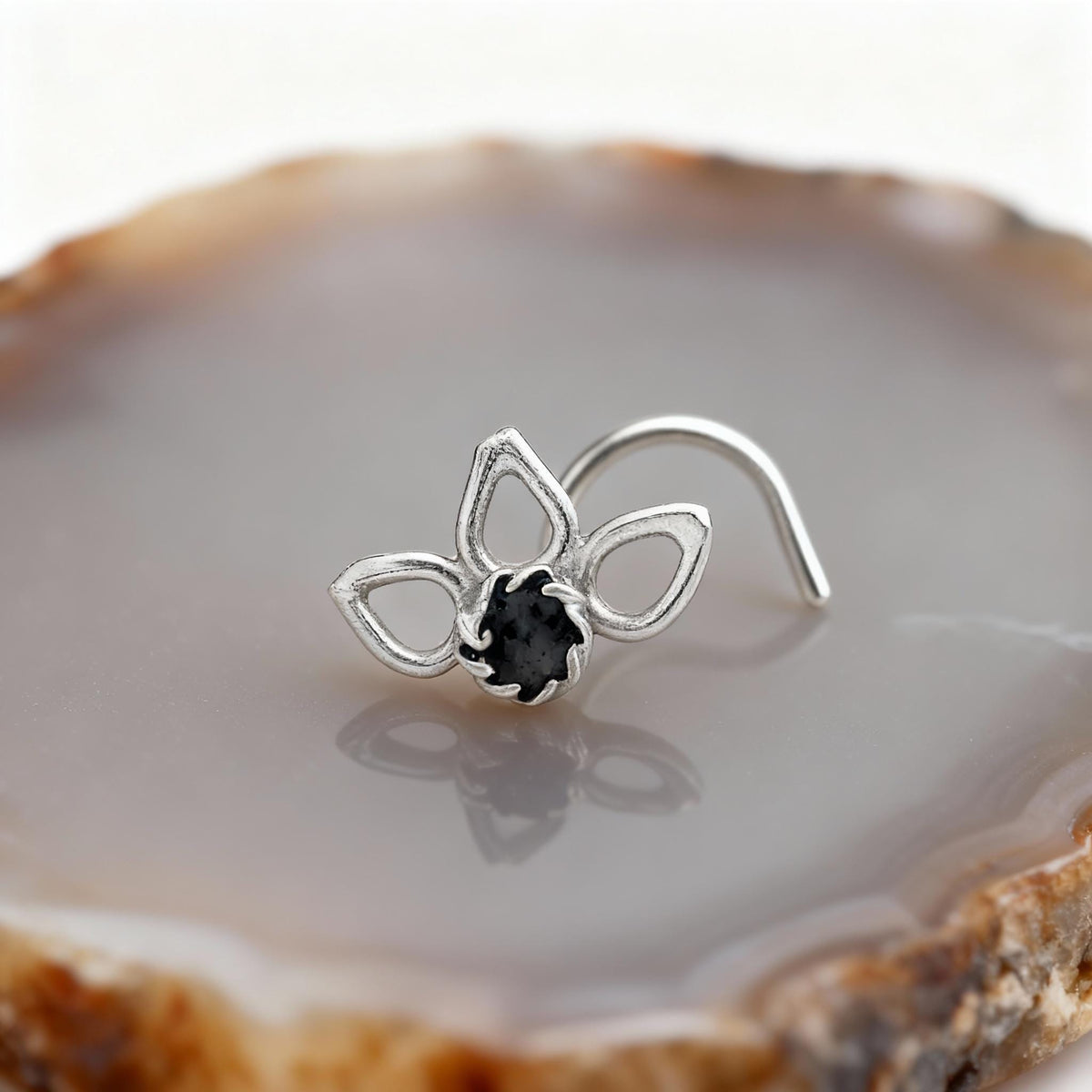 A silver nose ring with a black gemstone is displayed on a stone surface.