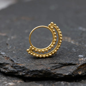 A gold-colored metal ring with a decorative design sits on a dark surface.