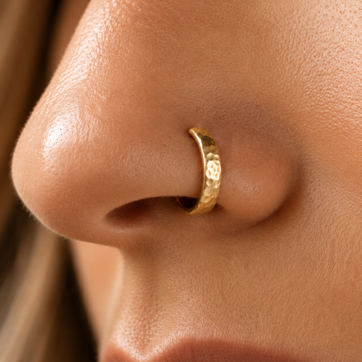 A close-up of a person's nose with a gold-colored nose ring.