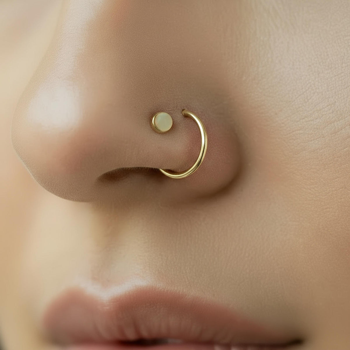 A close-up of a person's nose with a gold hoop earring attached.