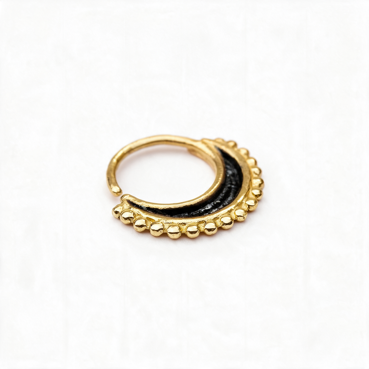 A gold-colored nose ring with a black crescent moon design and small gold-colored beads around the edge.