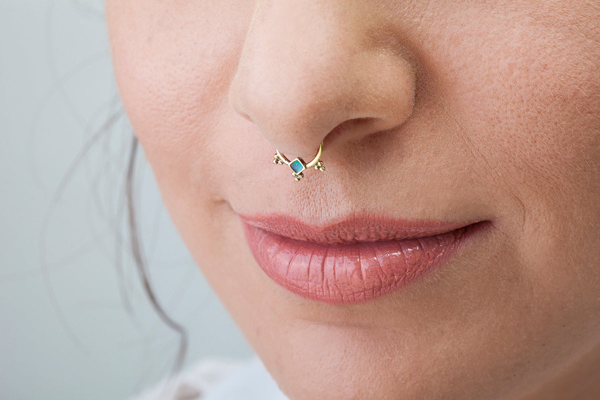 A close-up of a woman's face, focusing on her nose and lips. She is wearing a nose ring with a decorative piece on it.